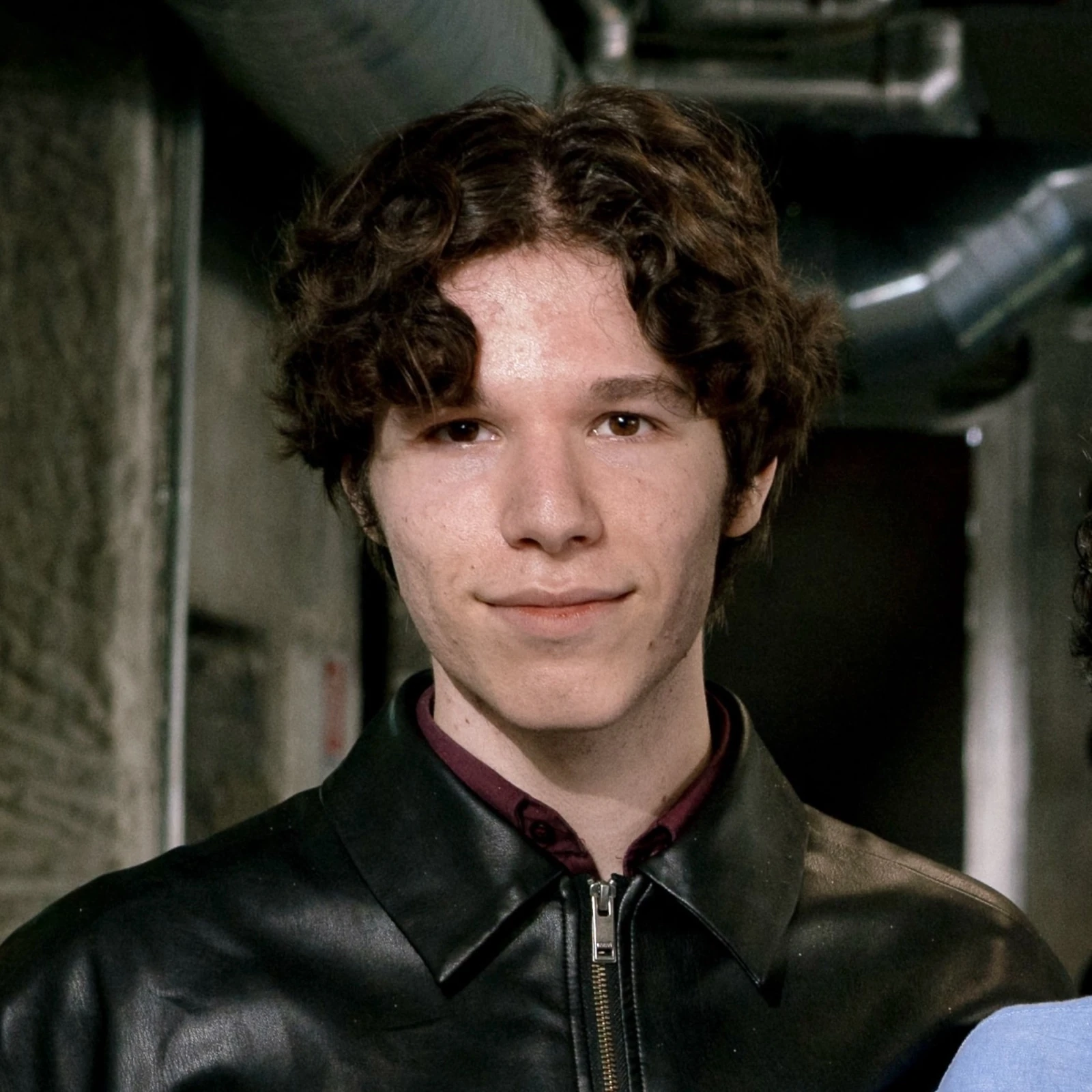Portrait of Ömer in a black leather jacket over a burgundy shirt, exposed ducting behind